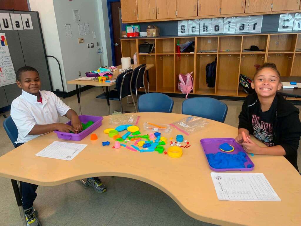 Two students are working with colorful sensory materials and tools at a classroom table.