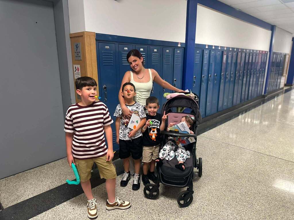 An adult woman and four young children are posing together in a school hallway.