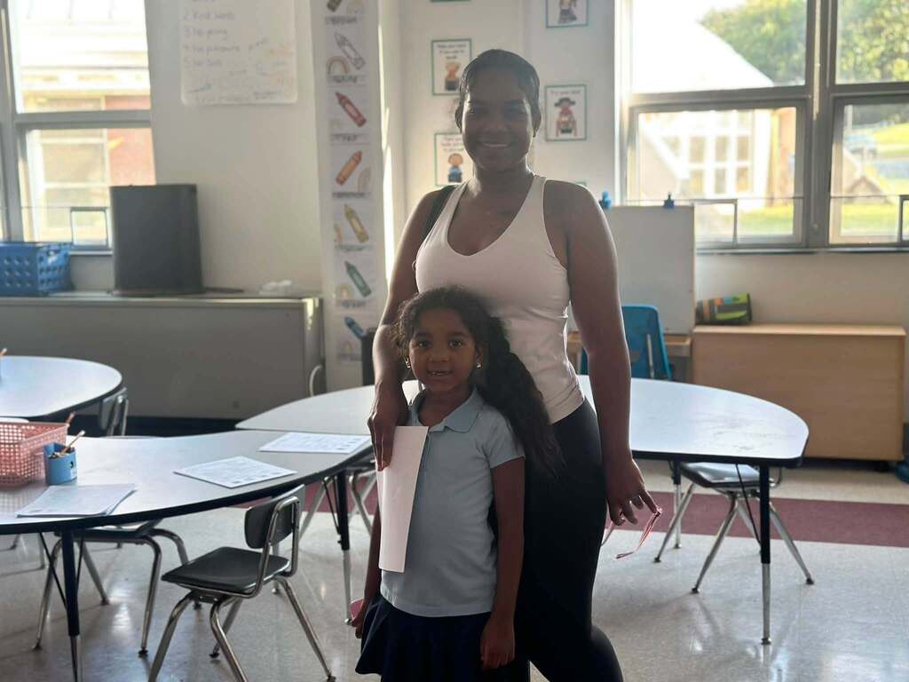 An adult and a young student are posing together in a school classroom.