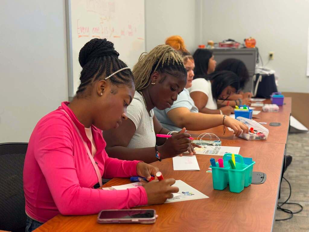 A group of students are sitting at a table in a learning lab, working on an activity that involves markers and papers.
