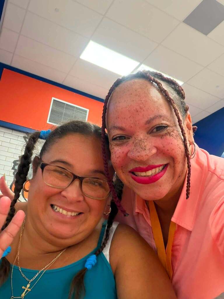 A district staff member is posing with a woman in a school cafeteria.