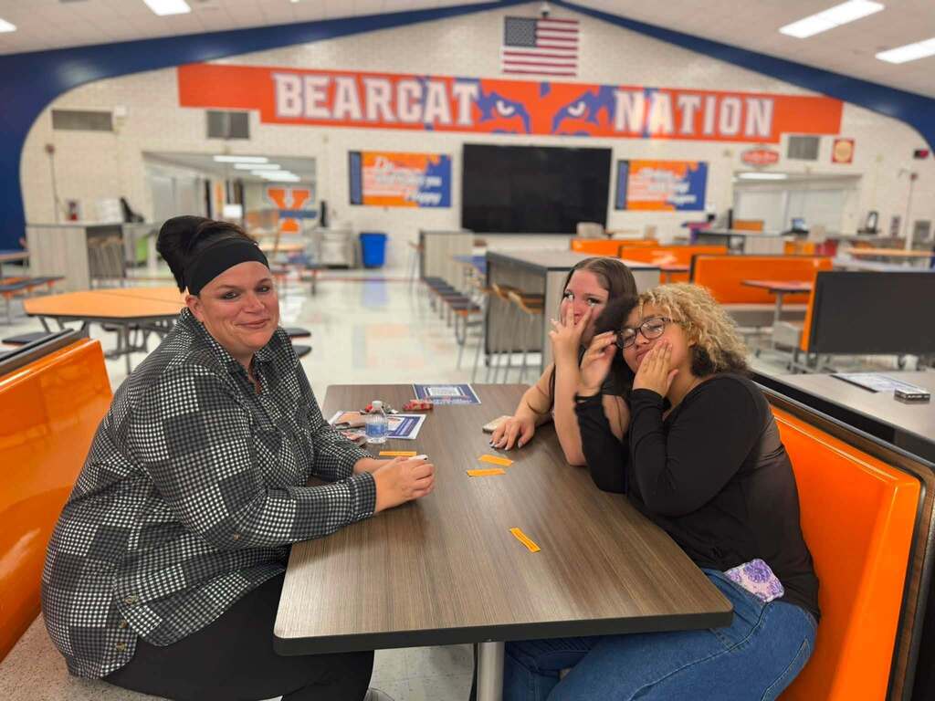 An adult and two students are sitting together at a table in a school cafeteria.