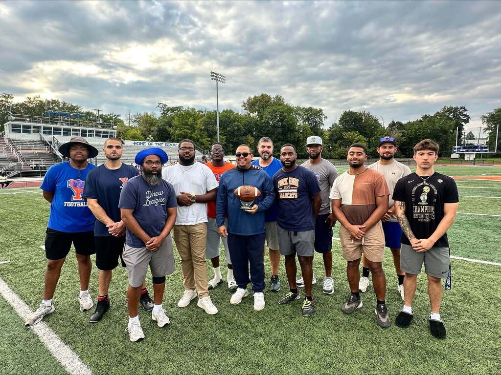A group of coaches and district staff members are posing together on a football field.