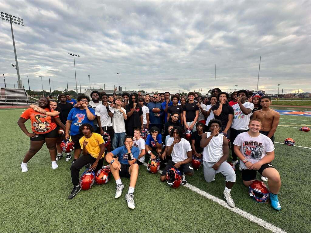 A large group of football players and coaches are posing together on a football field.