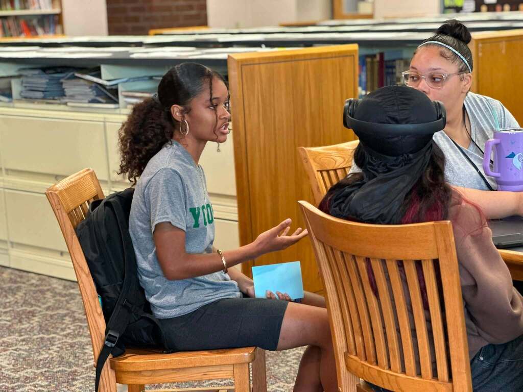 Dr. Andrea Berry-Brown, Superintendent of Schools, engaged in a student-led discussion with a group of William Penn Senior High School students in a school library.