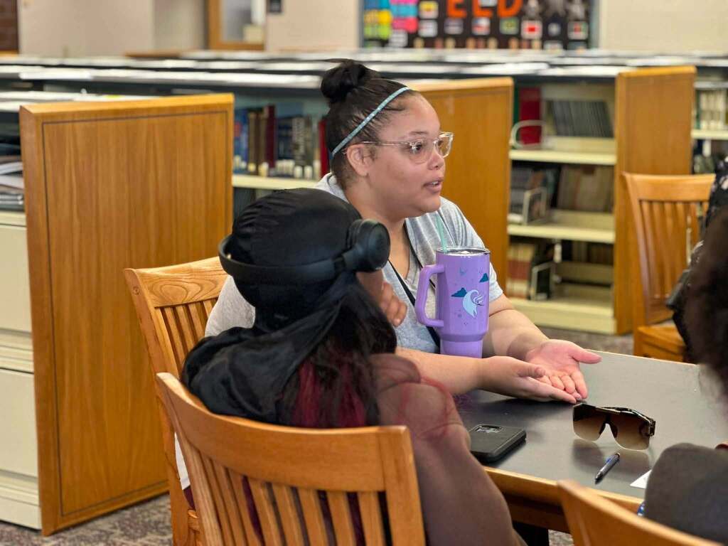 Dr. Andrea Berry-Brown, Superintendent of Schools, engaged in a student-led discussion with a group of William Penn Senior High School students in a school library.