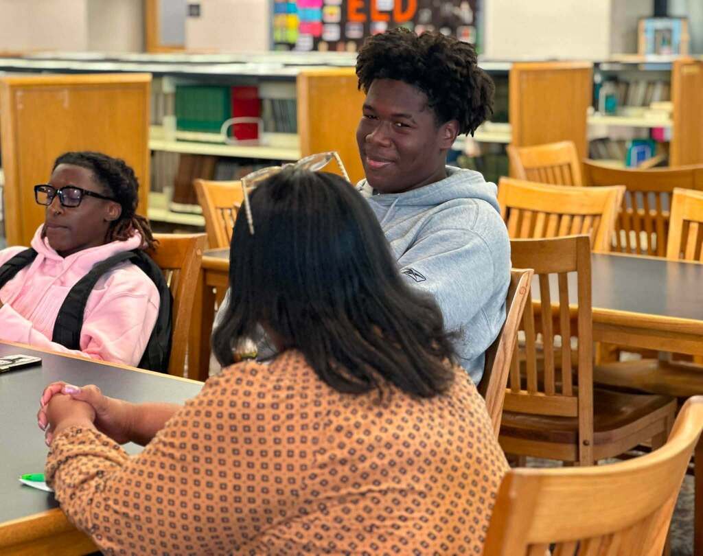 Dr. Andrea Berry-Brown, Superintendent of Schools, engaged in a student-led discussion with a group of William Penn Senior High School students in a school library.