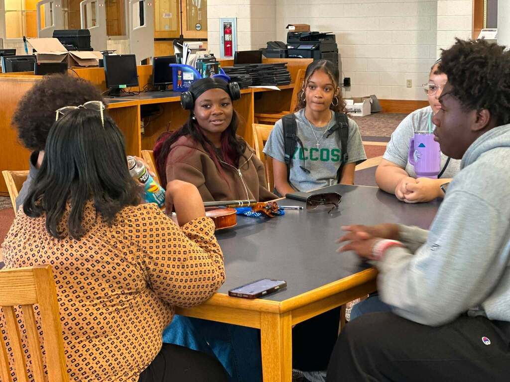 Dr. Andrea Berry-Brown, Superintendent of Schools, engaged in a student-led discussion with a group of William Penn Senior High School students in a school library.