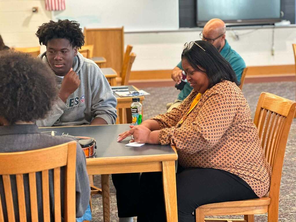 Dr. Andrea Berry-Brown, Superintendent of Schools, engaged in a student-led discussion with a group of William Penn Senior High School students in a school library.
