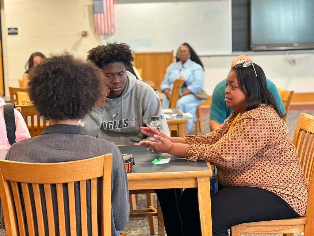 Dr. Andrea Berry-Brown, Superintendent of Schools, engaged in a student-led discussion with a group of William Penn Senior High School students in a school library.