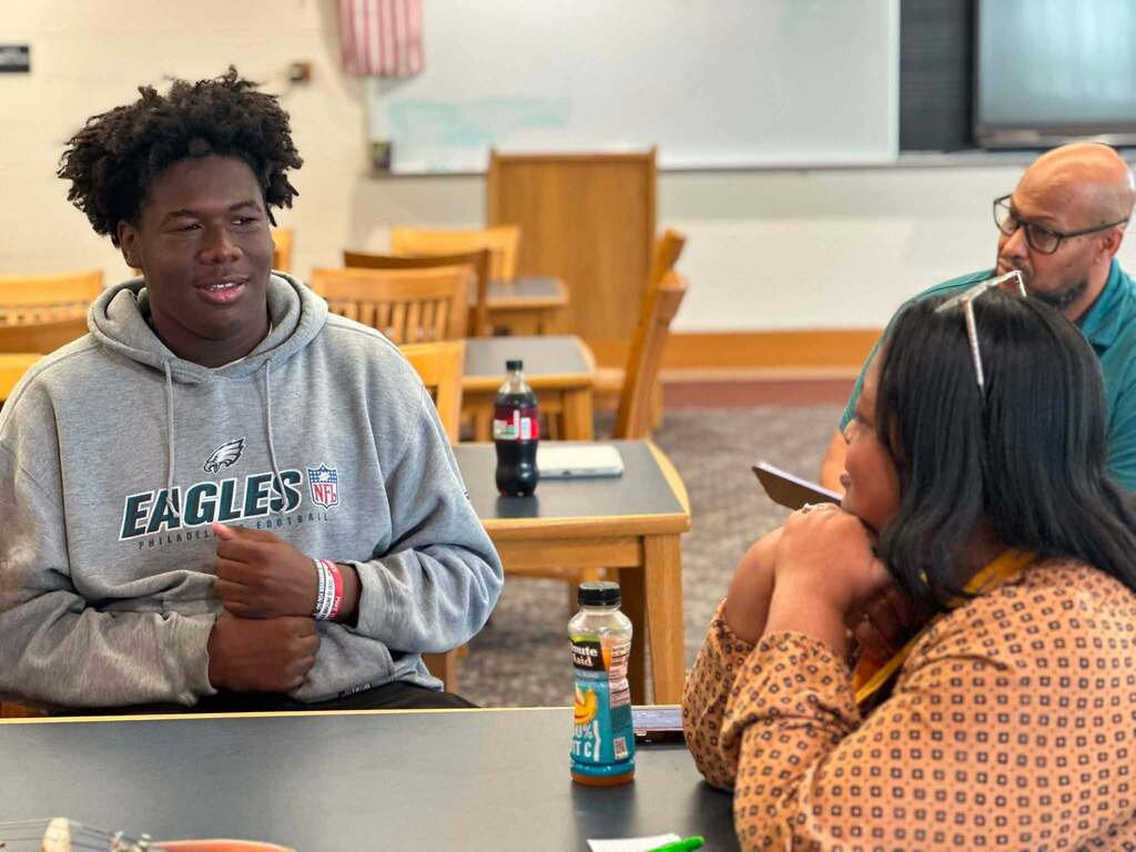 Dr. Andrea Berry-Brown, Superintendent of Schools, engaged in a student-led discussion with a group of William Penn Senior High School students in a school library.