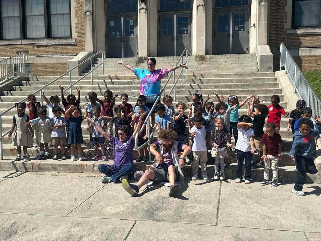 District students, staff and local community members are sitting and standing on the steps at Smith STEAM Academy. Confetti is being thrown in the air.