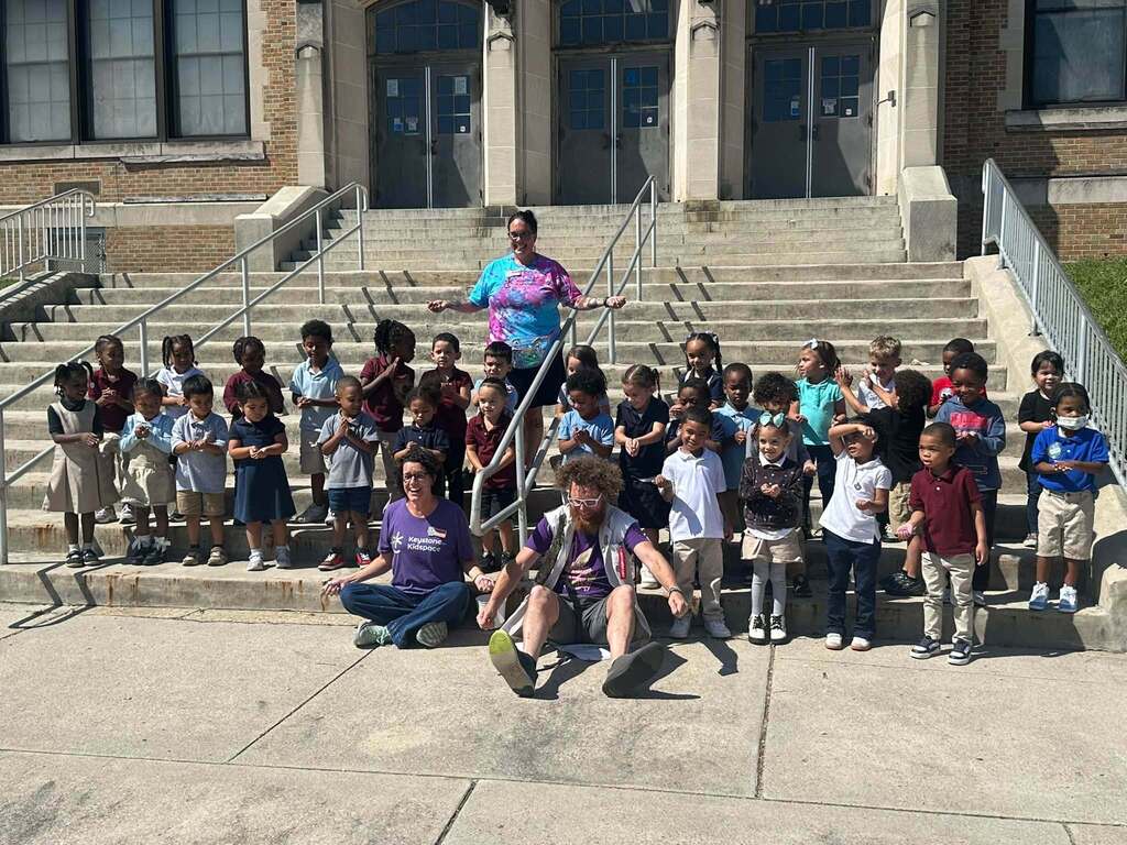 District students, staff and local community members are sitting and standing on the steps at Smith STEAM Academy. 
