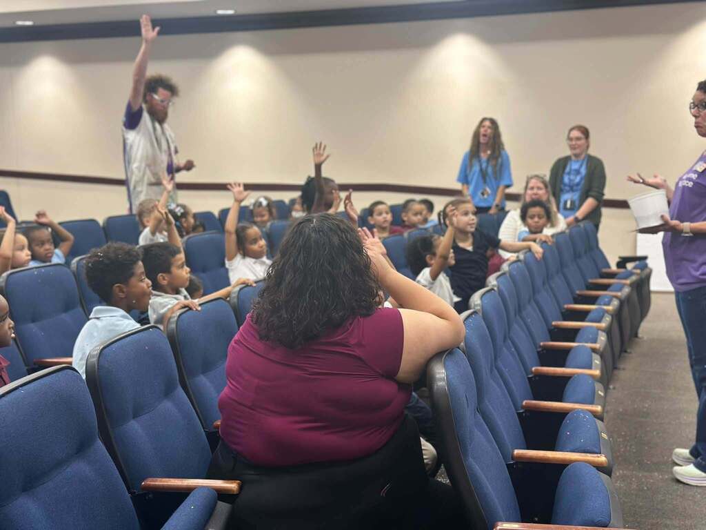 District students, staff and local community members are gathered in a school auditorium. 