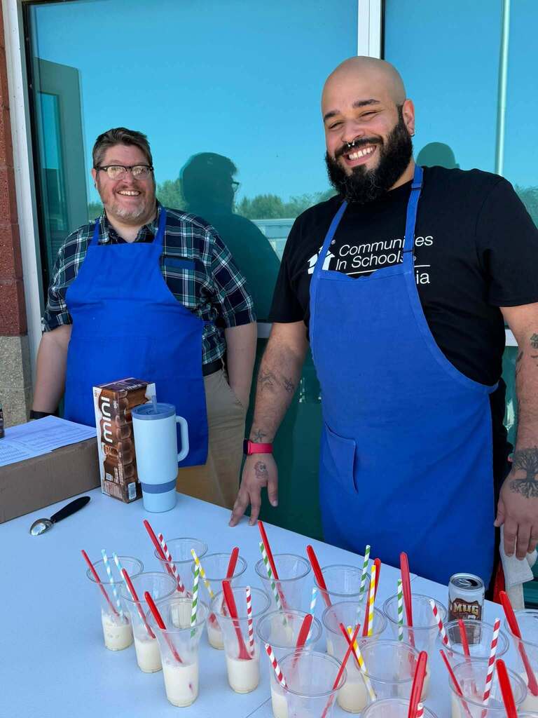 Two district staff members are standing behind a table that has root beer floats and a Stanley Cup on it.