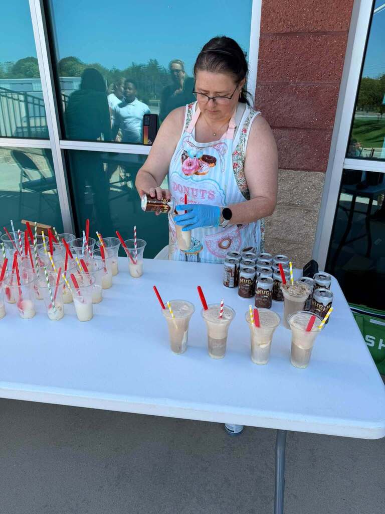 A district administrator is preparing root beer floats outdoors at a table. 