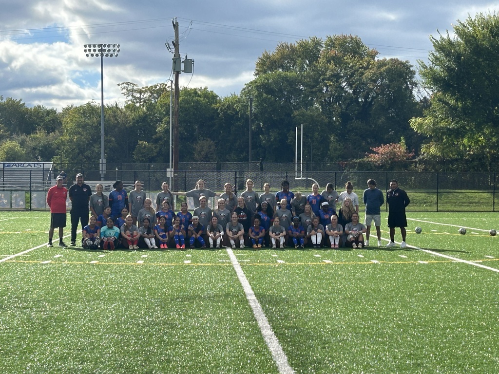 A large soccer team is posing for a group photo on an outdoor turf field.