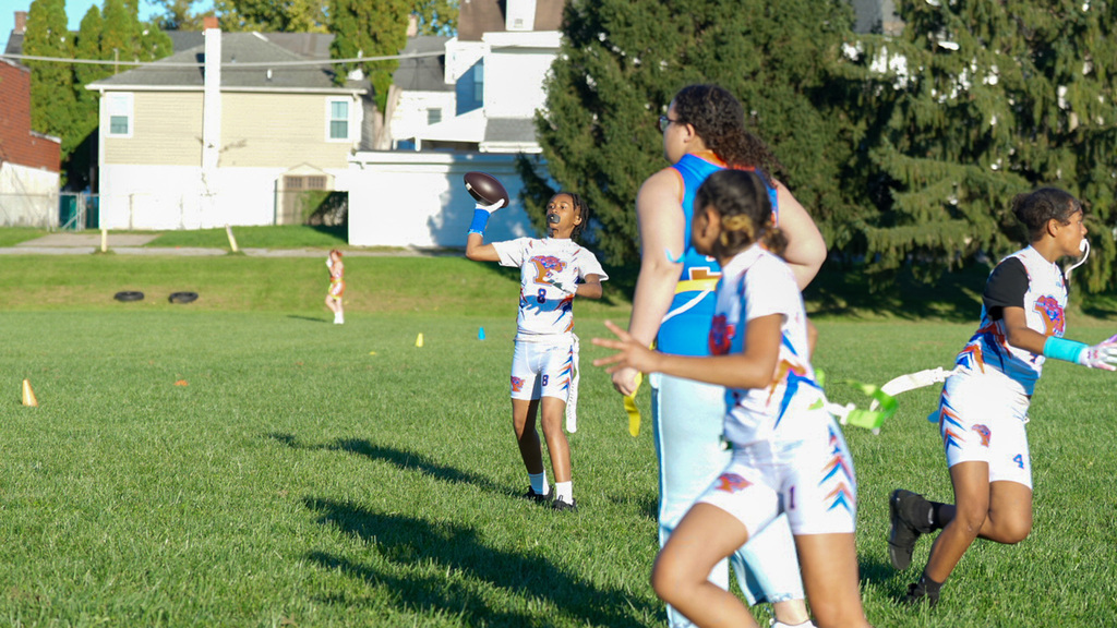SDCY middle school girls flag football players are competing in a flag football game on a field.