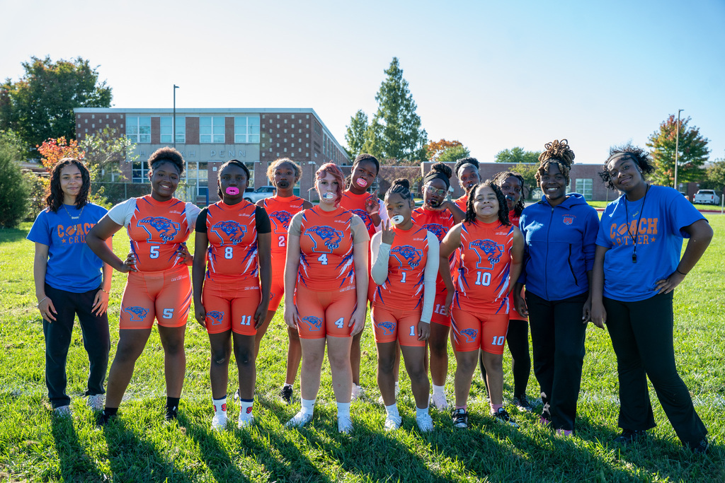 SDCY middle school girls flag football players and coaches are posing for a team photo on a field.