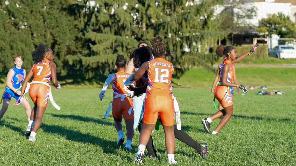 SDCY middle school girls flag football players are competing in a flag football game on a field.