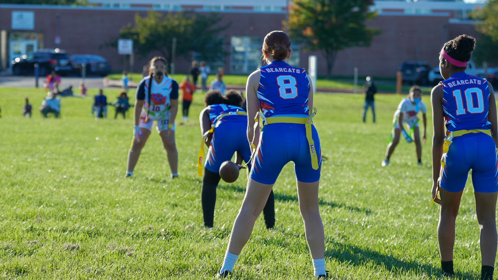 SDCY middle school girls flag football players are competing in a flag football game on a field.