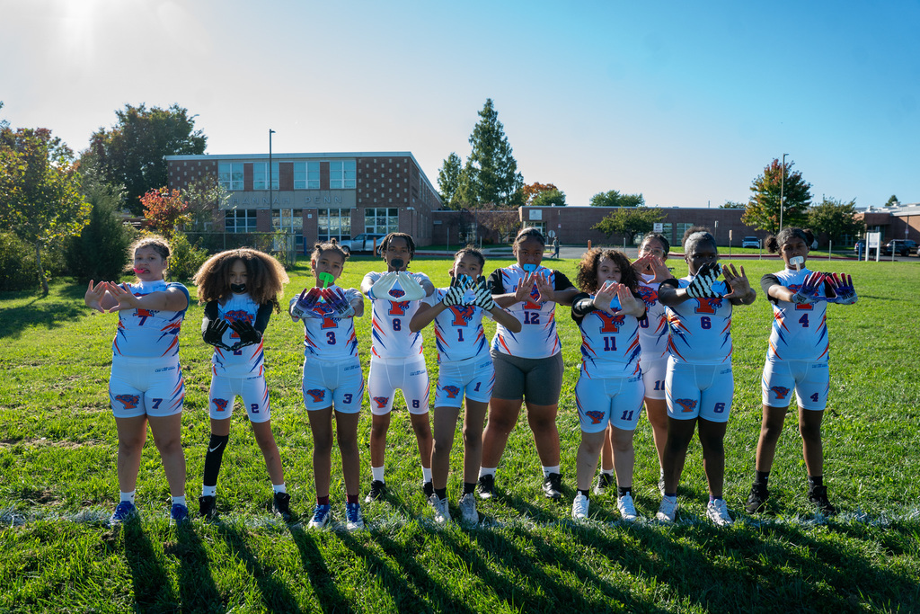 SDCY middle school girls flag football players and coaches are posing for a team photo on a field.
