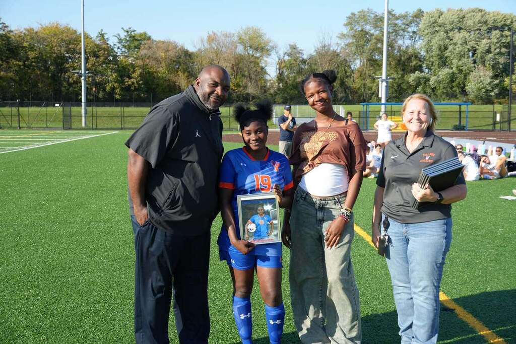 A William Penn girls’ soccer senior is posing with a family member and district staff members, while holding a framed photo during Senior Night.