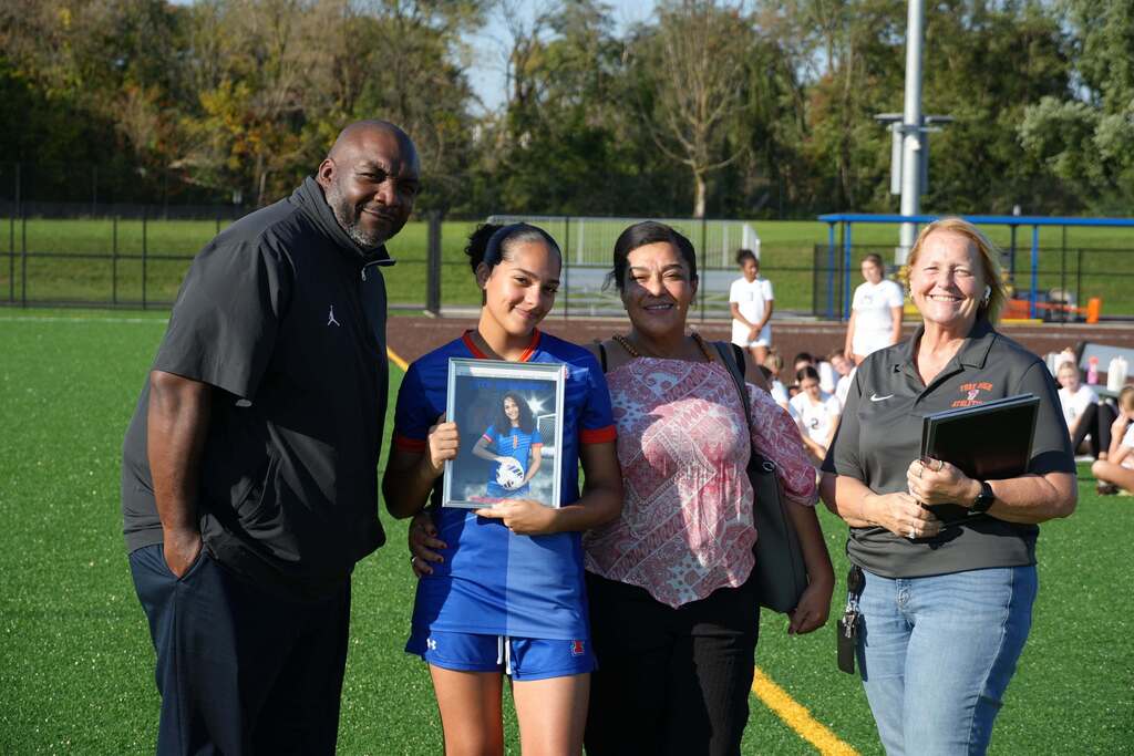 A William Penn girls’ soccer senior is posing with a family member and district staff members, while holding a framed photo during Senior Night.