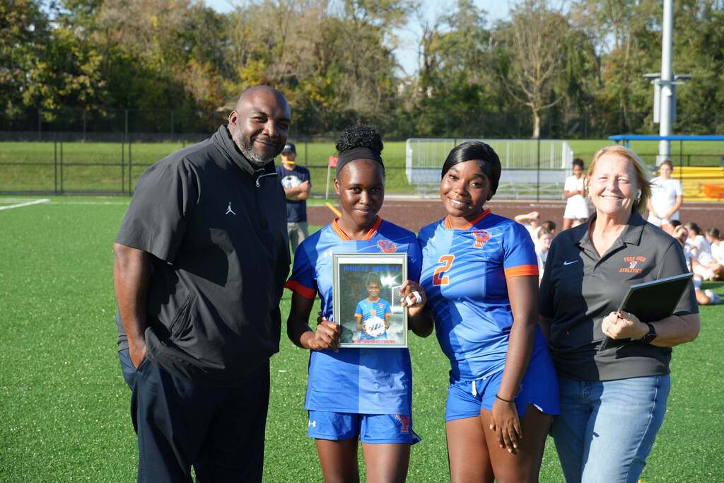 A William Penn girls’ soccer senior is posing with a teammate and district staff members, while holding a framed photo during Senior Night.