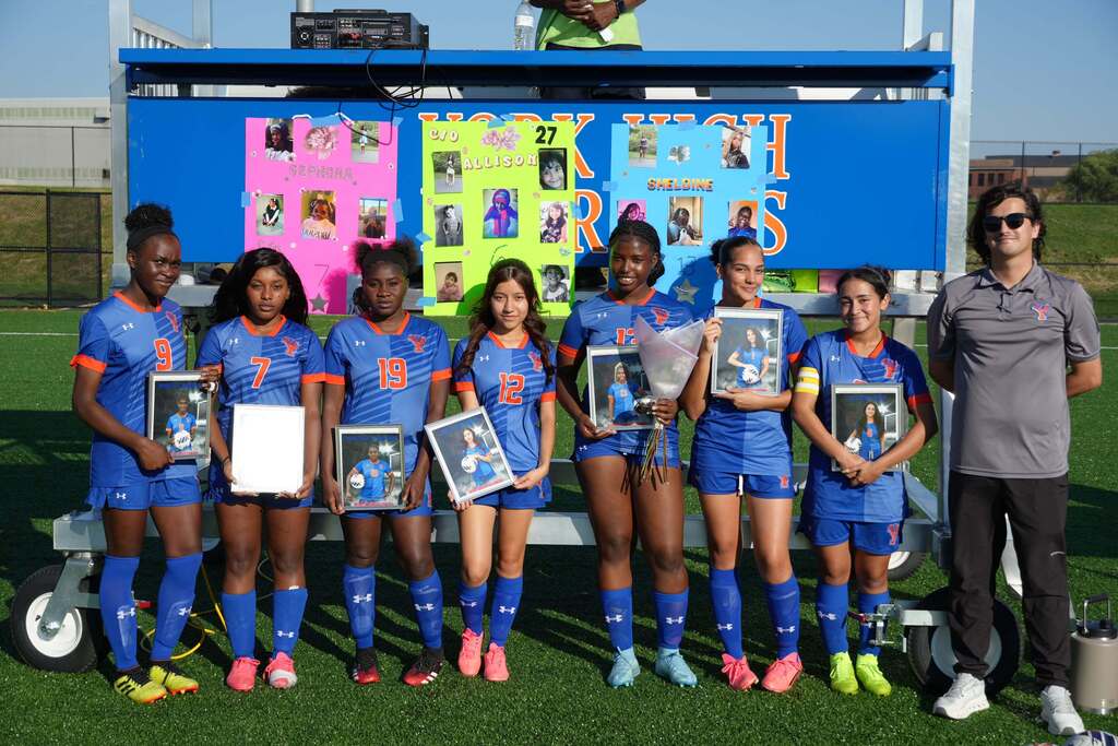 William Penn girls’ soccer players are posing with framed photos and flowers during Senior Night alongside their coach.
