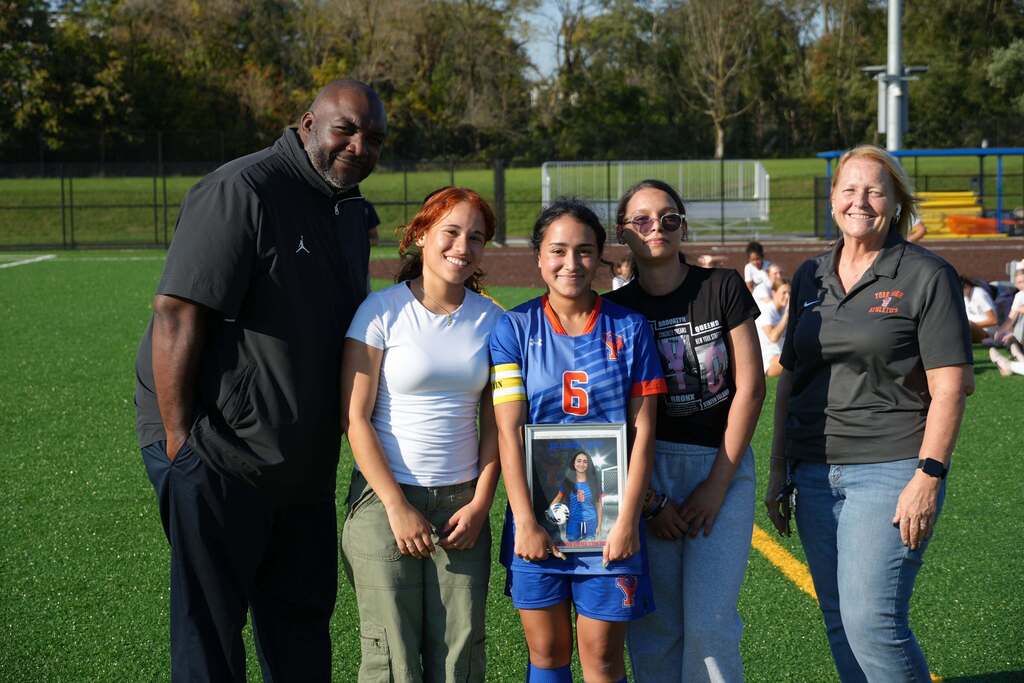 A William Penn girls’ soccer senior is posing with family members and district staff members, while holding a framed photo during Senior Night.