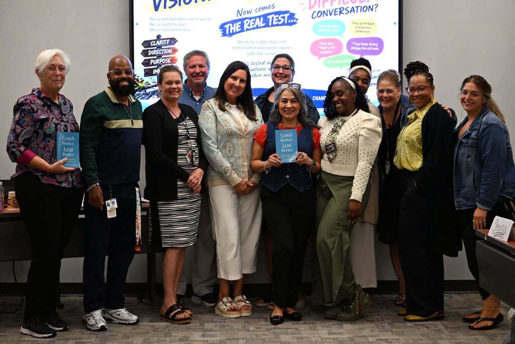 A group of district Network Coaches are posing together after a professional development session featuring the book Coach Better, Lead Better.