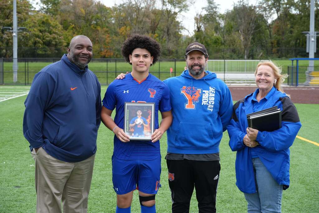 A William Penn boys' soccer senior is posing with district staff members, while holding a framed photo during Senior Night.