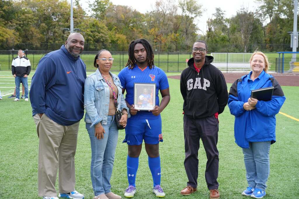 A William Penn boys' soccer senior is posing with family members and district staff members, while holding a framed photo during Senior Night.