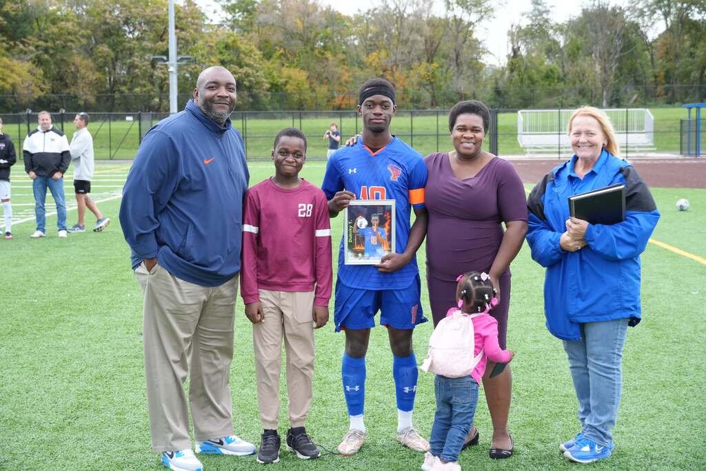 A William Penn boys' soccer senior is posing with family members and district staff members, while holding a framed photo during Senior Night.