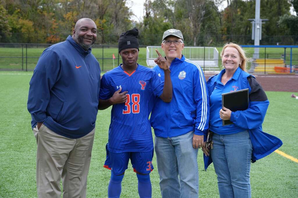 A William Penn boys' soccer senior is posing with district staff members and local community members.
