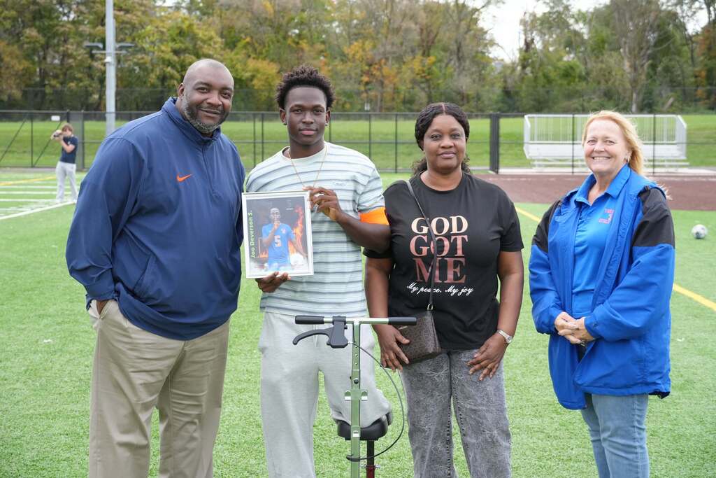 A William Penn boys' soccer senior is posing with a family member and district staff members, while holding a framed photo during Senior Night.