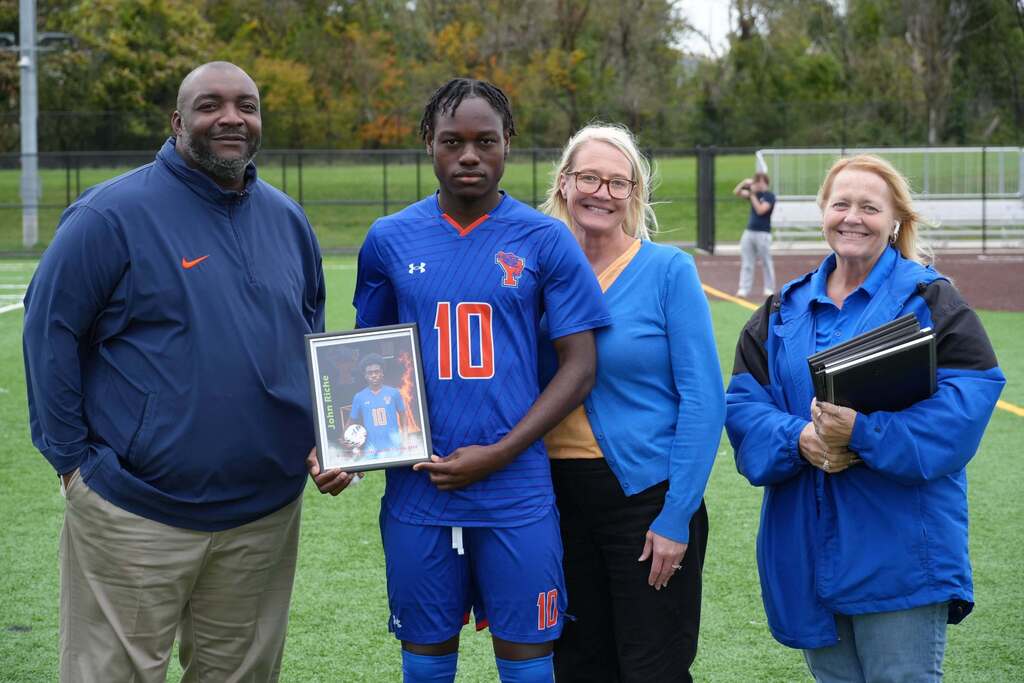 A William Penn boys' soccer senior is posing with district staff members, while holding a framed photo during Senior Night.