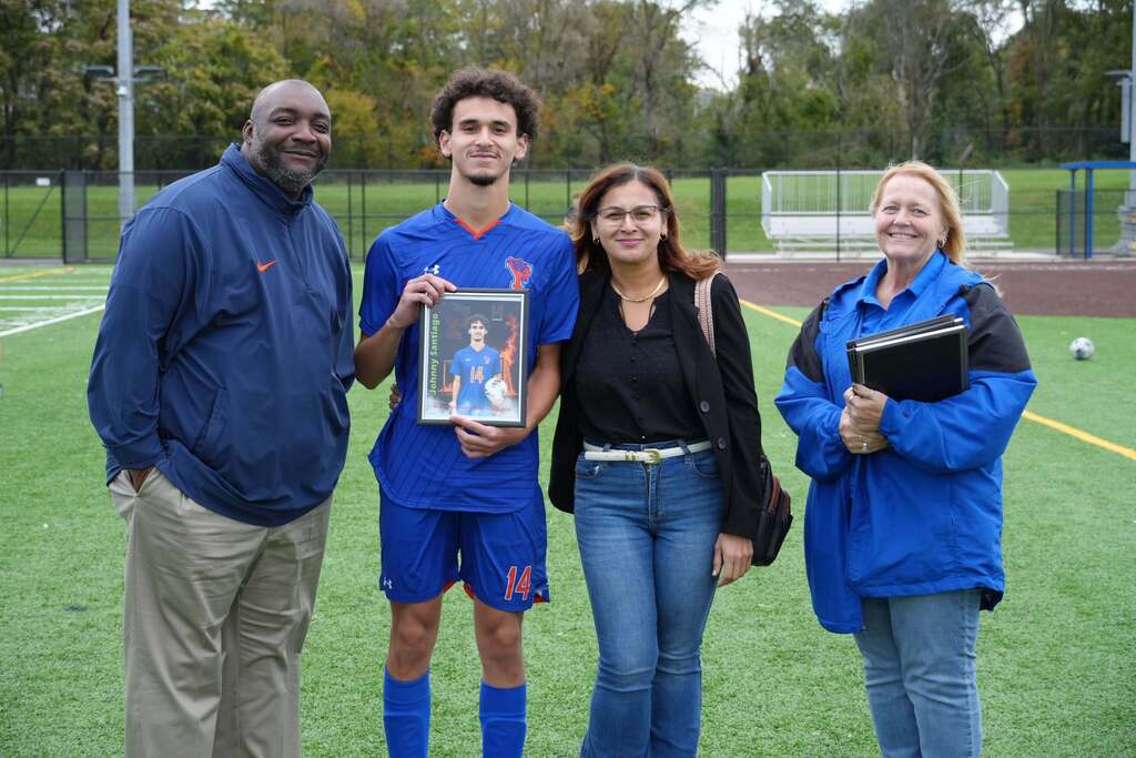 A William Penn boys' soccer senior is posing with a family member and district staff members, while holding a framed photo during Senior Night.