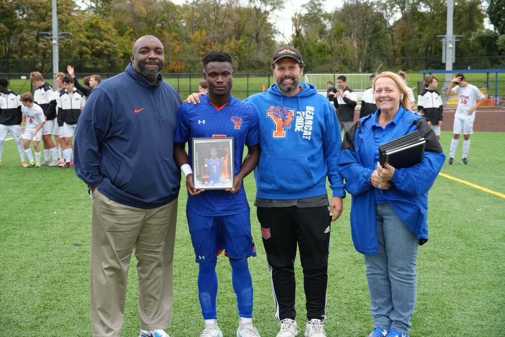 A William Penn boys' soccer senior is posing with district staff members, while holding a framed photo during Senior Night.