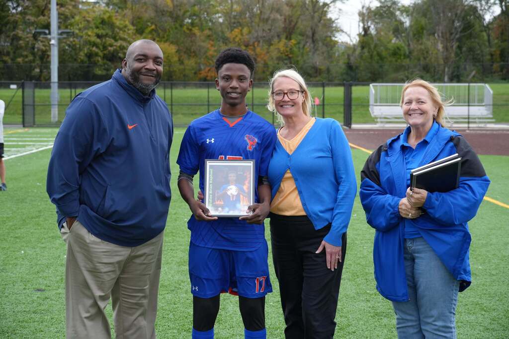 A William Penn boys' soccer senior is posing with district staff members, while holding a framed photo during Senior Night.