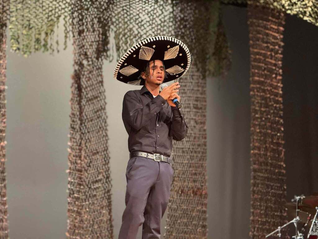 A student wearing a traditional sombrero is singing into a microphone during a Hispanic Heritage Month celebration.