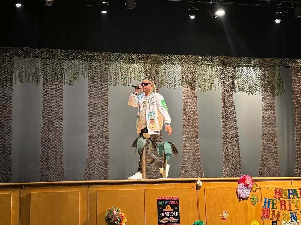 A performer is singing into a microphone onstage during a Hispanic Heritage Month celebration.