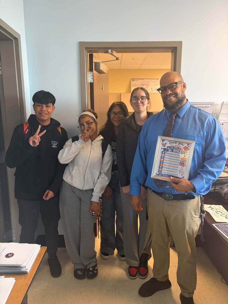 Four students are posing with their principal who is holding a framed thank-you gift in an office area.