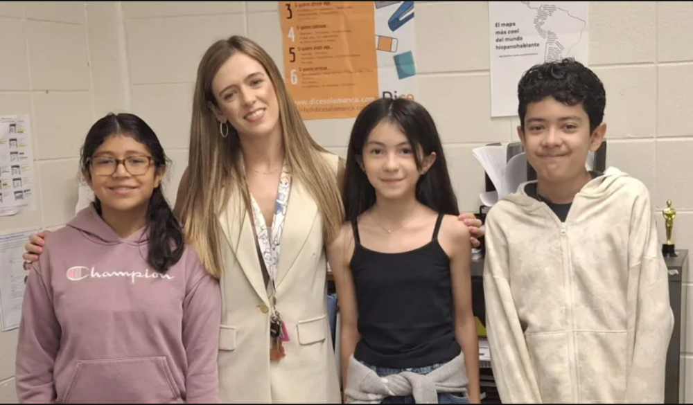 A young female teacher puts her arms around three middle school students. They all are smiling.