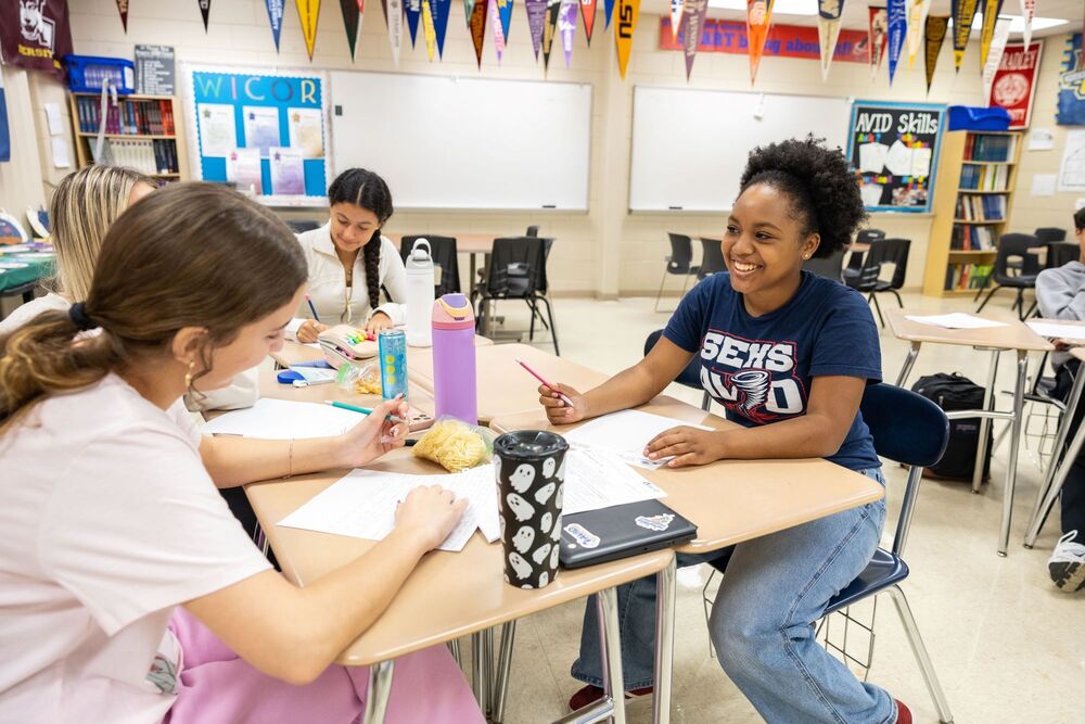 A group of high school students work together in a classroom. College pennants hang from the ceiling.