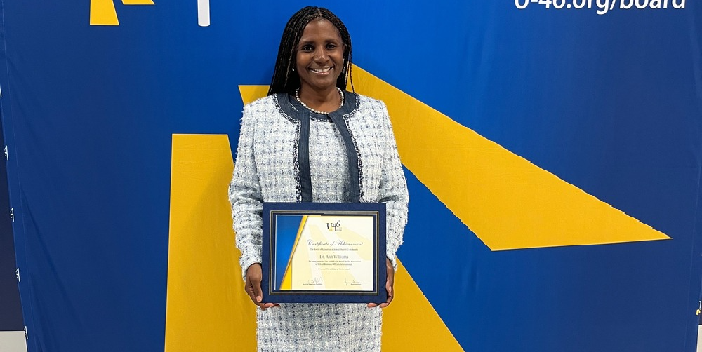 A woman stands in front of a sign with an award