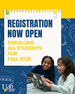 Two students look at a laptop with a sign in the background. The sign reads "Registration Now Open".