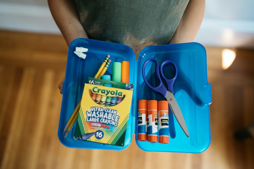 Child holds a pencil box filled with common school supplies.
