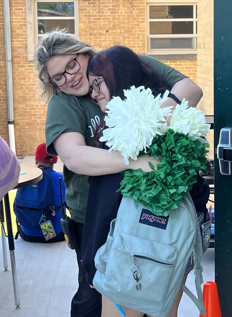 Two individuals hugging, one holding a bouquet of white flowers and green pom-poms. 